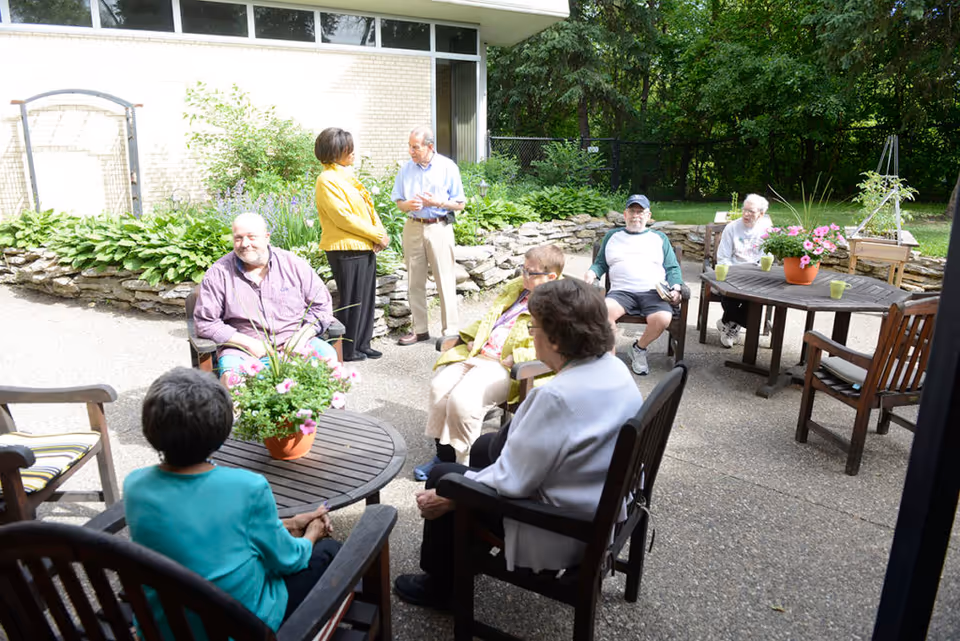 Group of seniors socializing on an outdoor patio with tables and potted flowers.