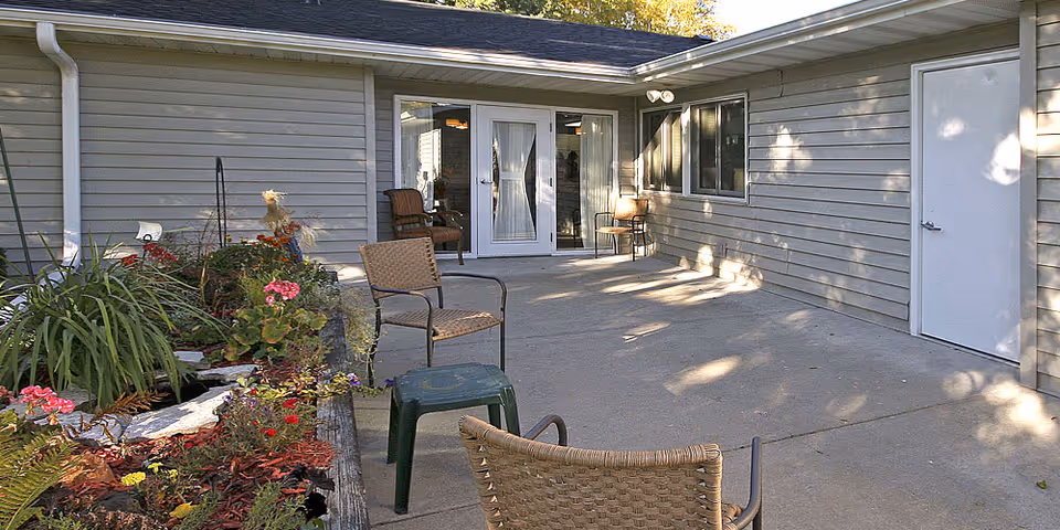 Concrete patio with wicker chairs and a planter of flowers outside sliding glass doors of the building.