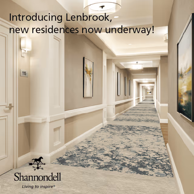 Long carpeted interior corridor of a senior living facility with doors, wall art, and ceiling lights.