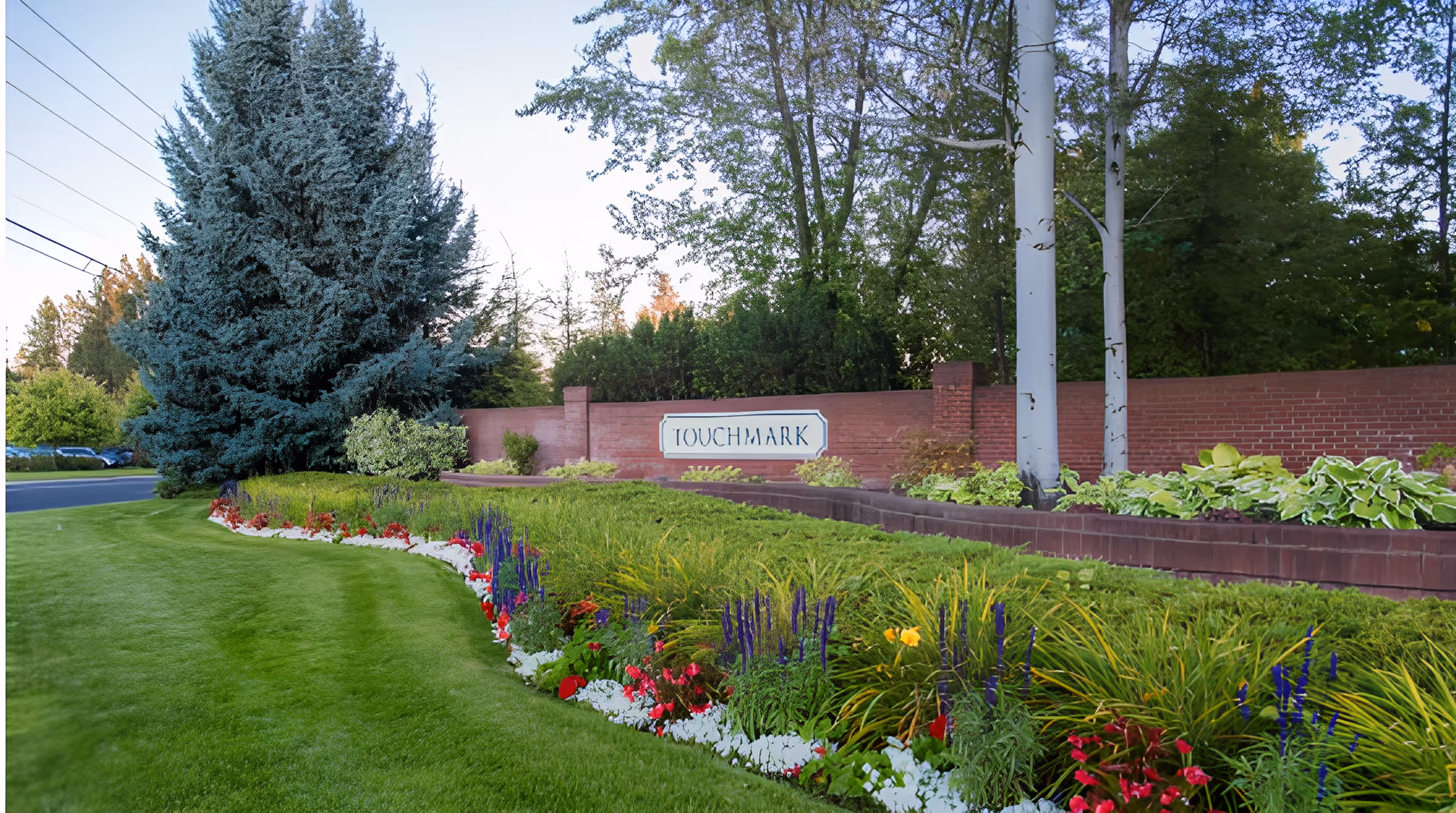 Landscaped lawn and colorful flowerbeds with a brick entrance wall and a sign reading 'Touchmark'.