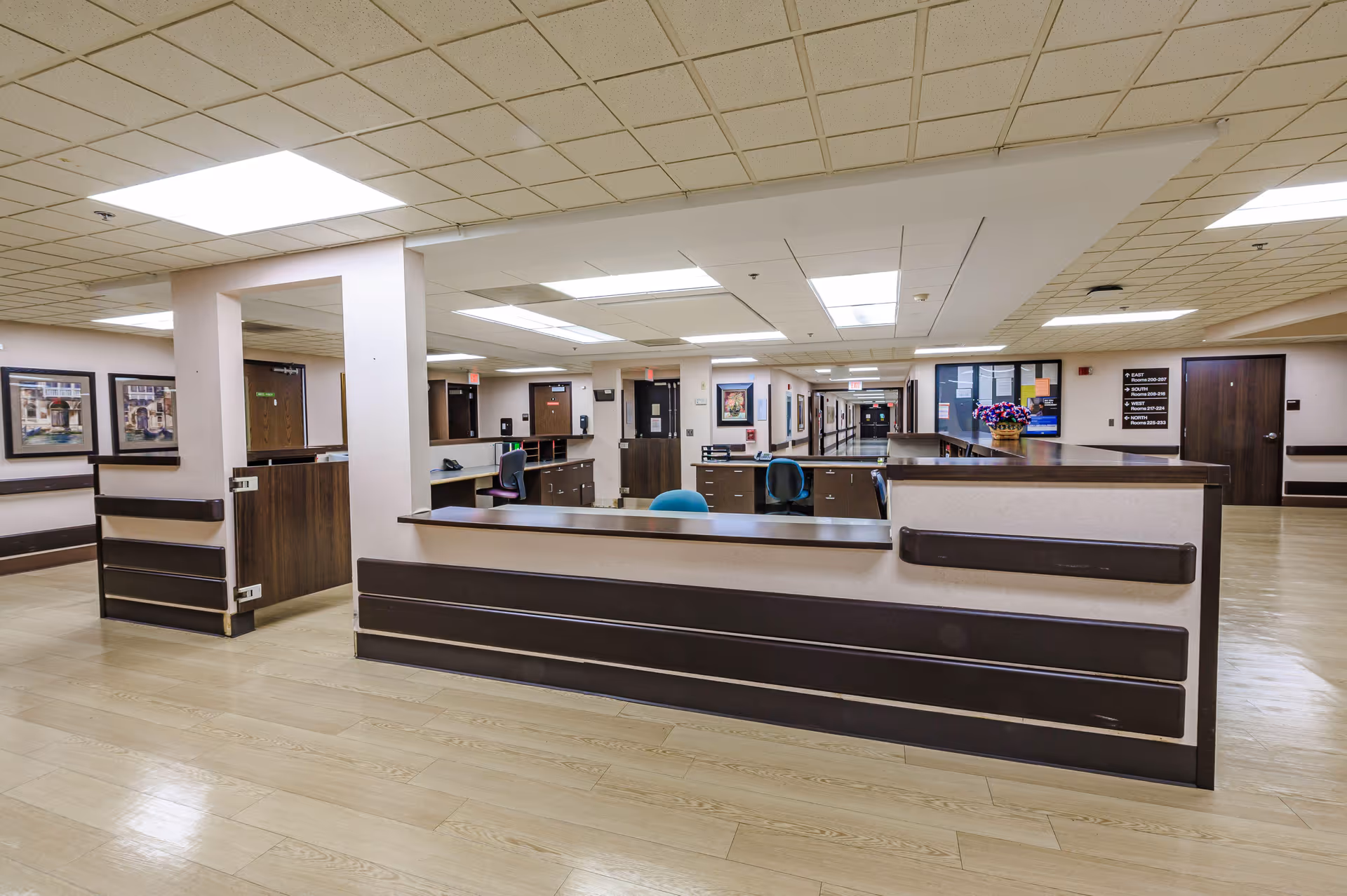 Reception and nurses' station with desks and chairs in a bright hallway of a senior living facility.