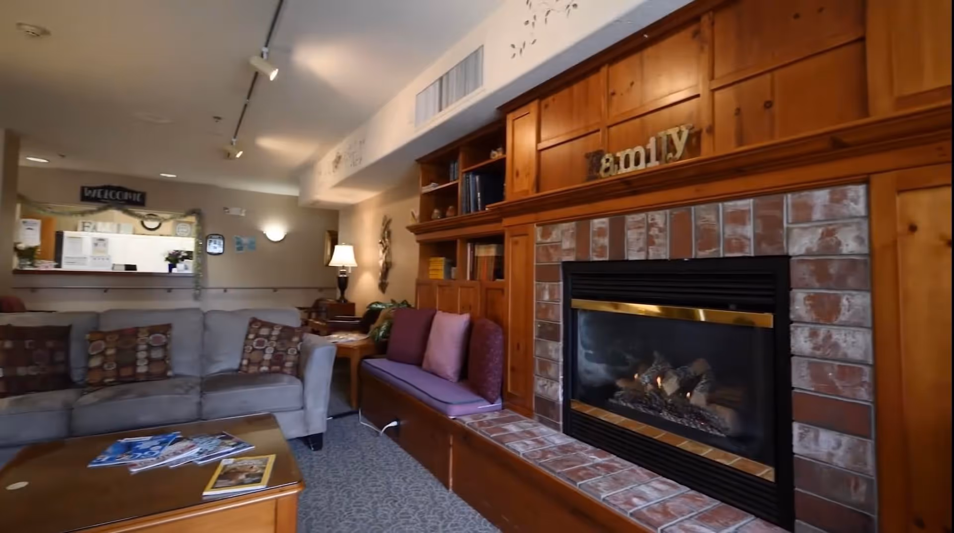 Cozy common-room lounge with sofas, built-in wooden shelving and a brick fireplace.