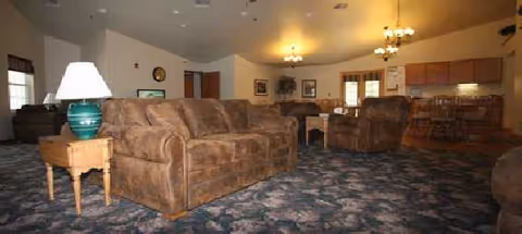 Cozy living room with brown sofas, a patterned carpet, and a dining area in back.