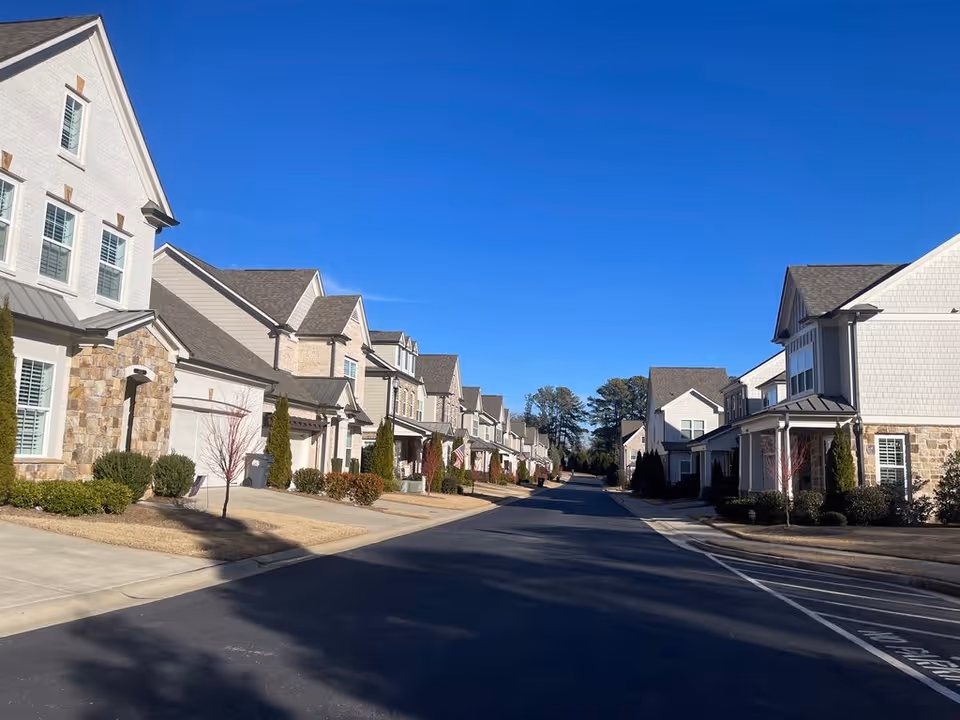 Row of townhouse-style residential buildings lining a quiet street under a clear blue sky.