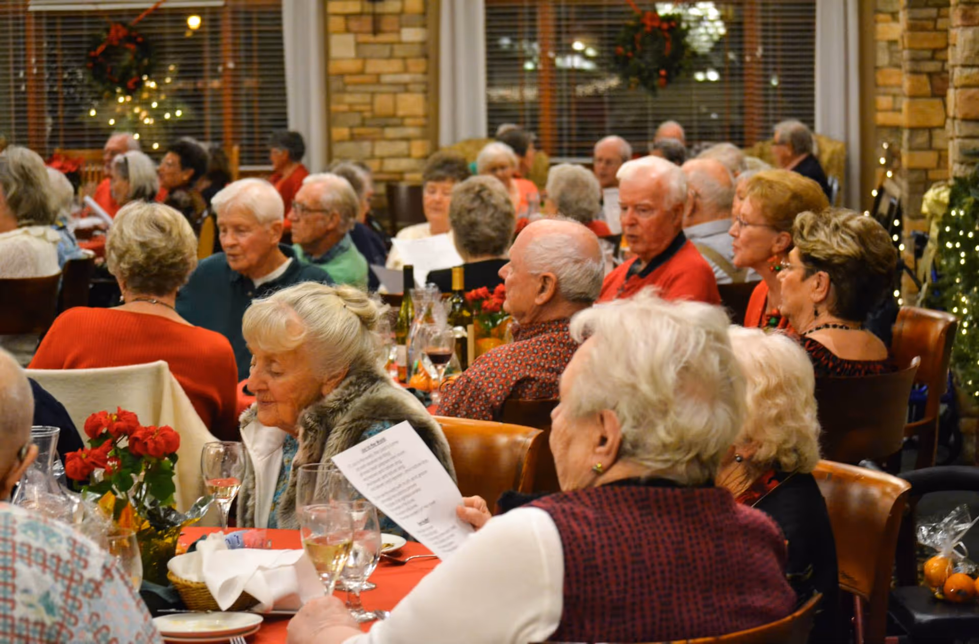 Elderly residents seated at decorated tables enjoying a communal holiday dinner in a dining room.