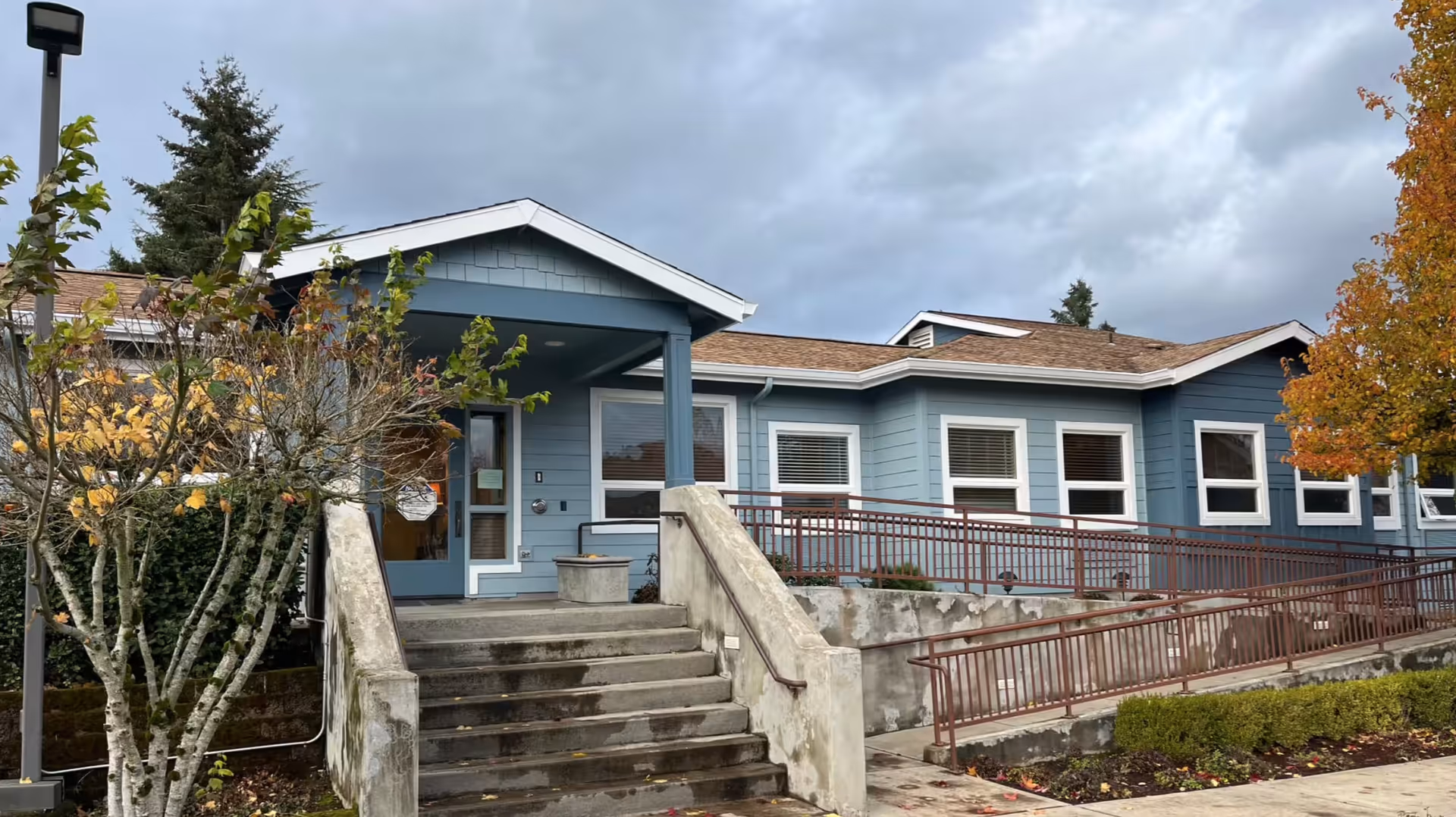 Blue single-story senior living facility exterior entrance with stairs and a ramp