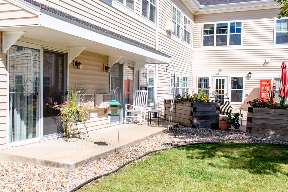 Sunny courtyard patio at a senior living facility with sliding glass doors, potted flowers, raised planters and outdoor seating.