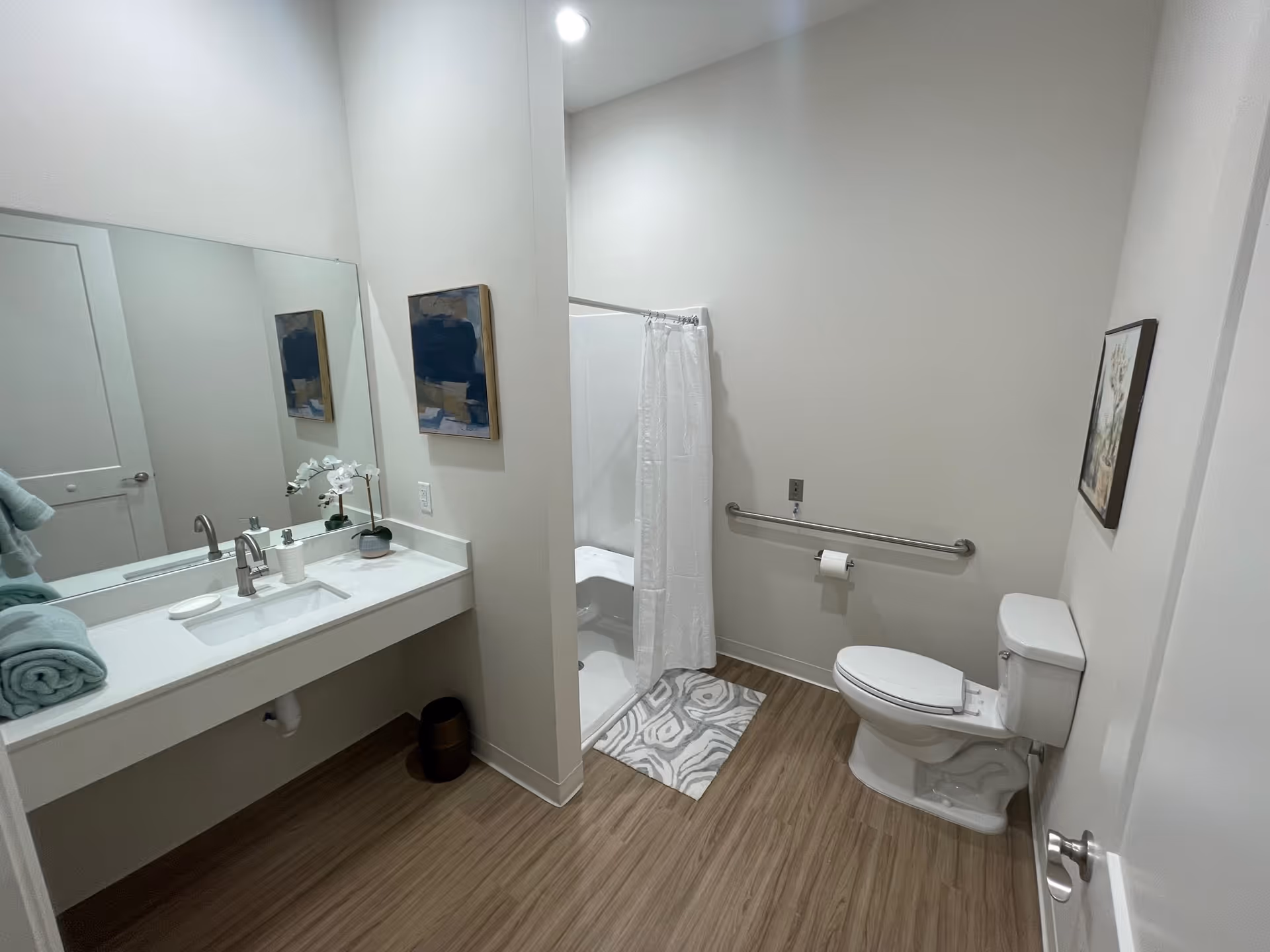 Bright accessible bathroom with a long vanity, shower, toilet, and grab bar.