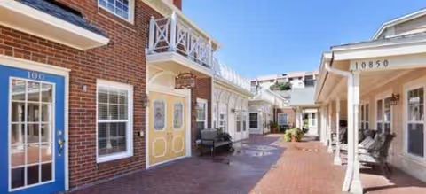 Outdoor courtyard of a senior living facility with brick path, storefront entrances, and seating.