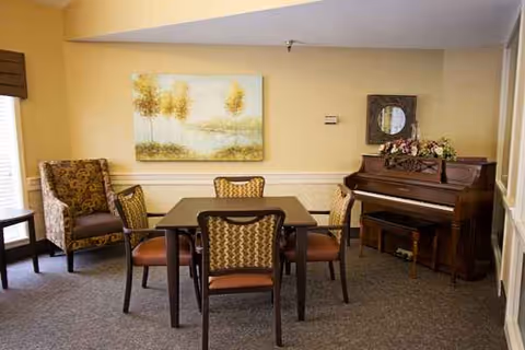 A cozy interior lounge with a dining table, chairs, piano, and wall art.