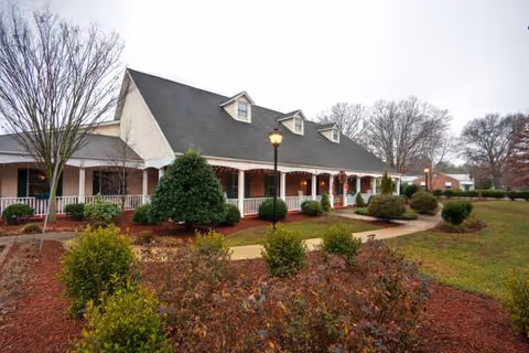 Long assisted-living building with a covered front porch, lampposts, and landscaped walkway.