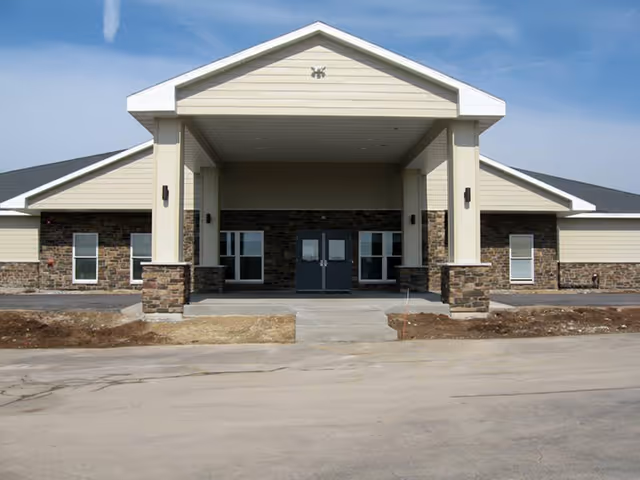 Front entrance of a single-story building with a covered portico, stone accents, and double doors.