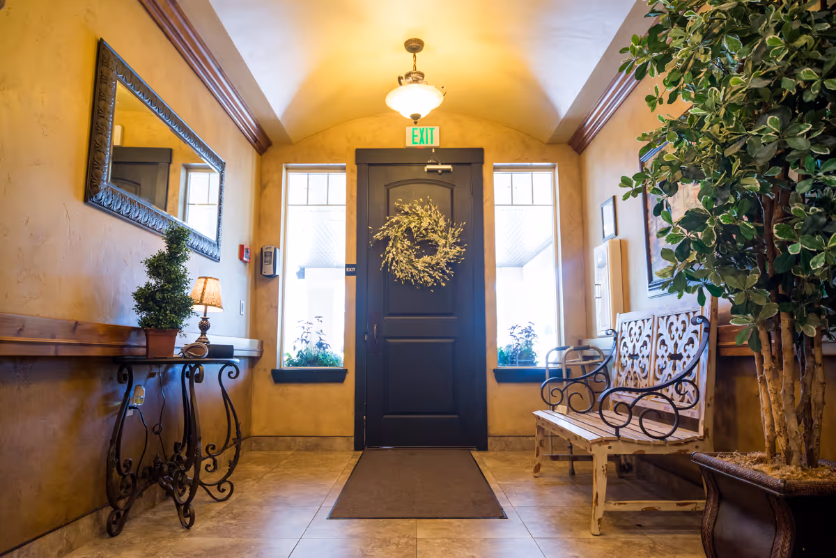 Entry foyer with a decorated front door and wreath, bench seating, console table with lamp and potted plants.