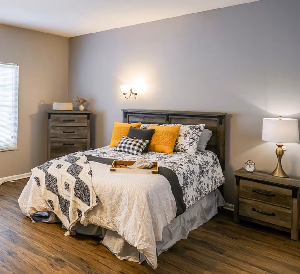 Cozy bedroom with a made bed, wooden headboard, nightstands with lamps, and a dresser.