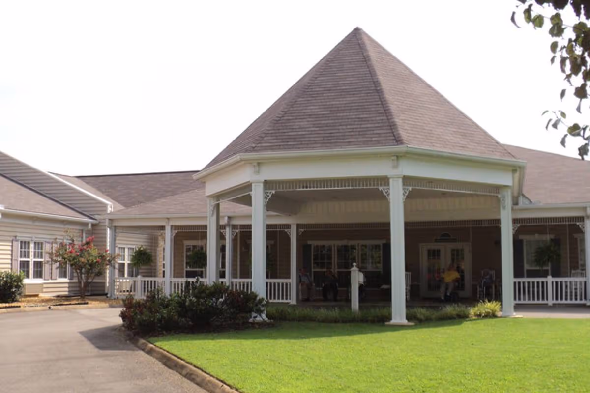 Exterior view of HarborChase of Jasper featuring a covered entrance with white columns and a peaked roof, surrounded by a well-maintained lawn and some shrubs.