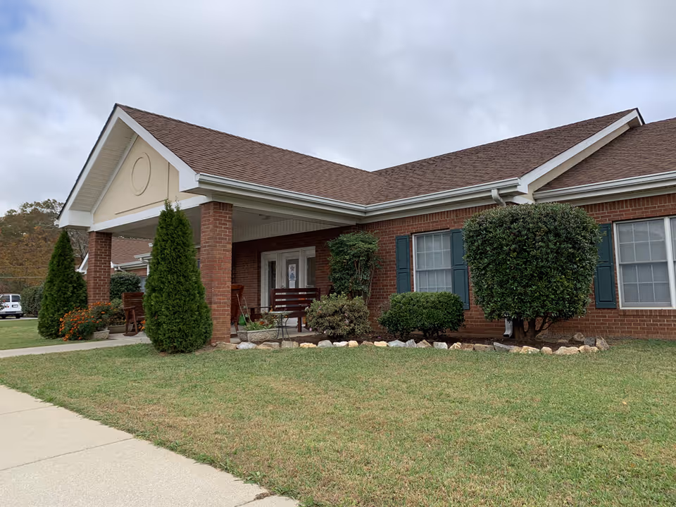 Brick senior living facility with a covered entrance, manicured shrubs, and a lawn.
