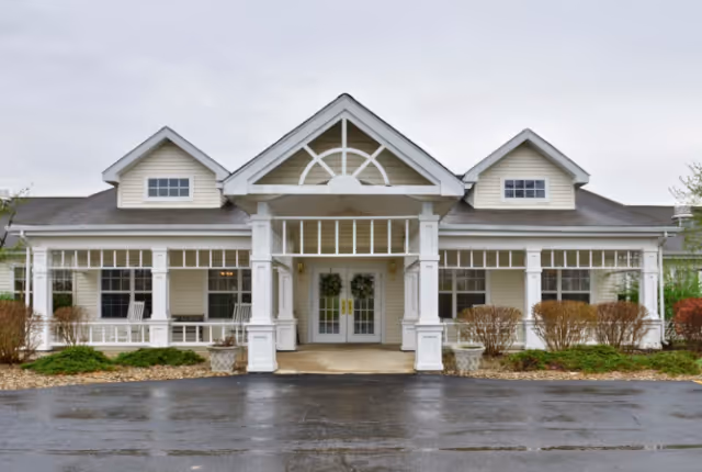 Front entrance of a single-story senior living building with white columns, a covered portico, and wreath-adorned double doors.