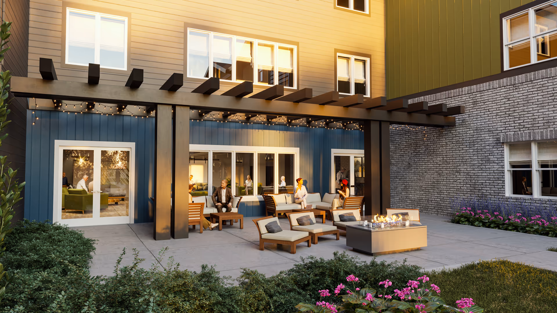Outdoor patio area at The Pointe at Meridian with seating arrangements including cushioned chairs and sofas around a fire pit. The patio is adjacent to the building with large windows and doors, and string lights are hung under a wooden pergola. There are plants and flowers bordering the patio area.