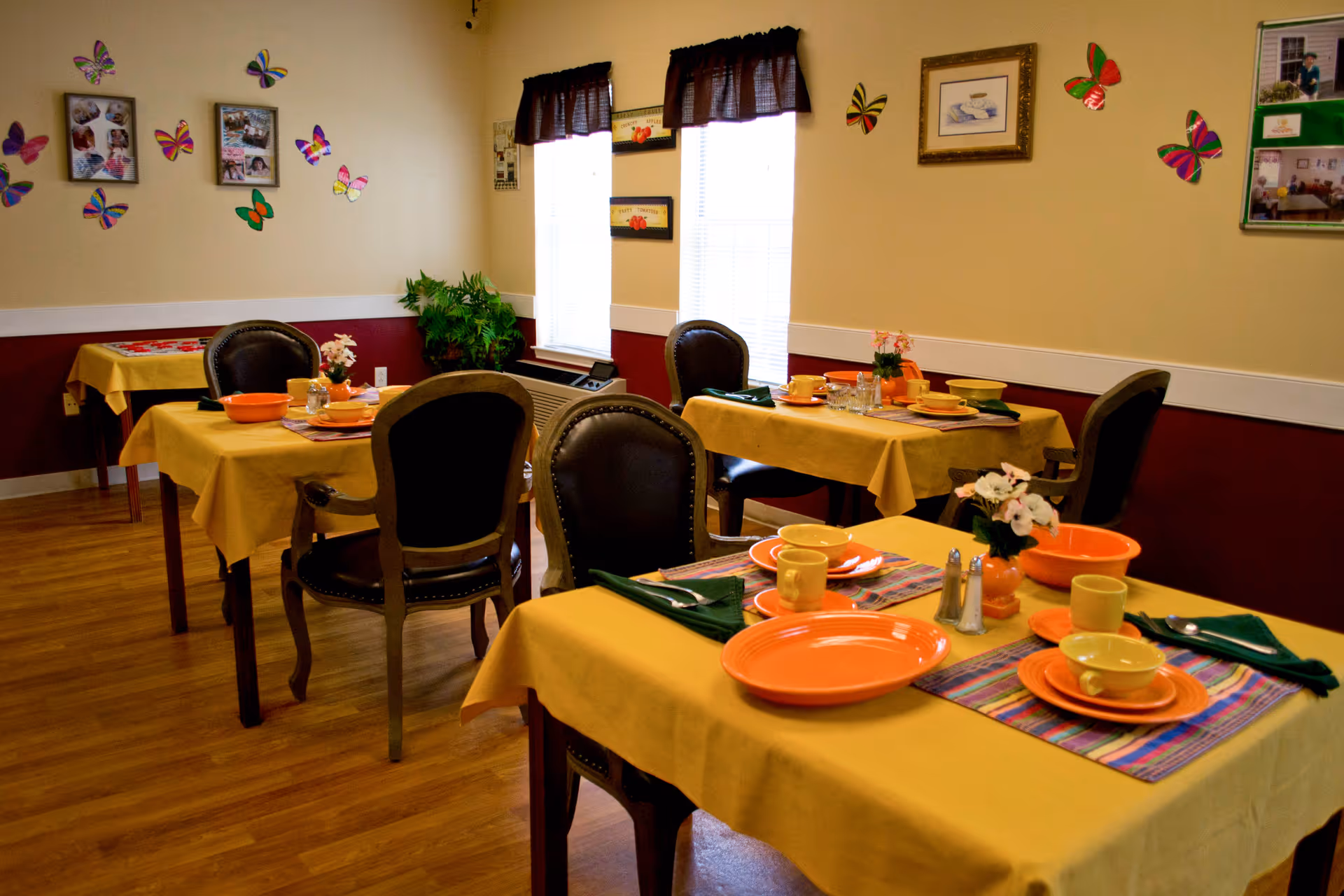 Dining room with several tables set with orange dishware and yellow tablecloths, chairs, and butterfly wall decorations.