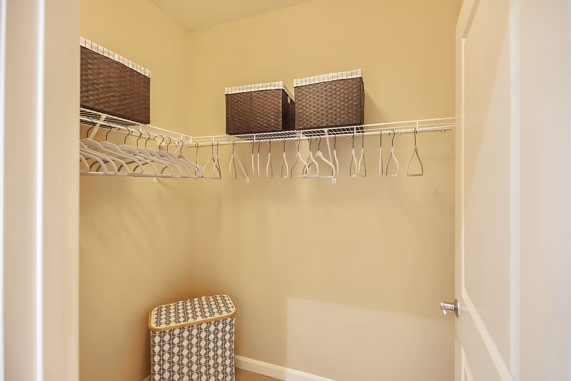 Walk-in closet with wire shelving, empty hangers, three woven storage baskets on the upper shelf and a patterned laundry hamper.