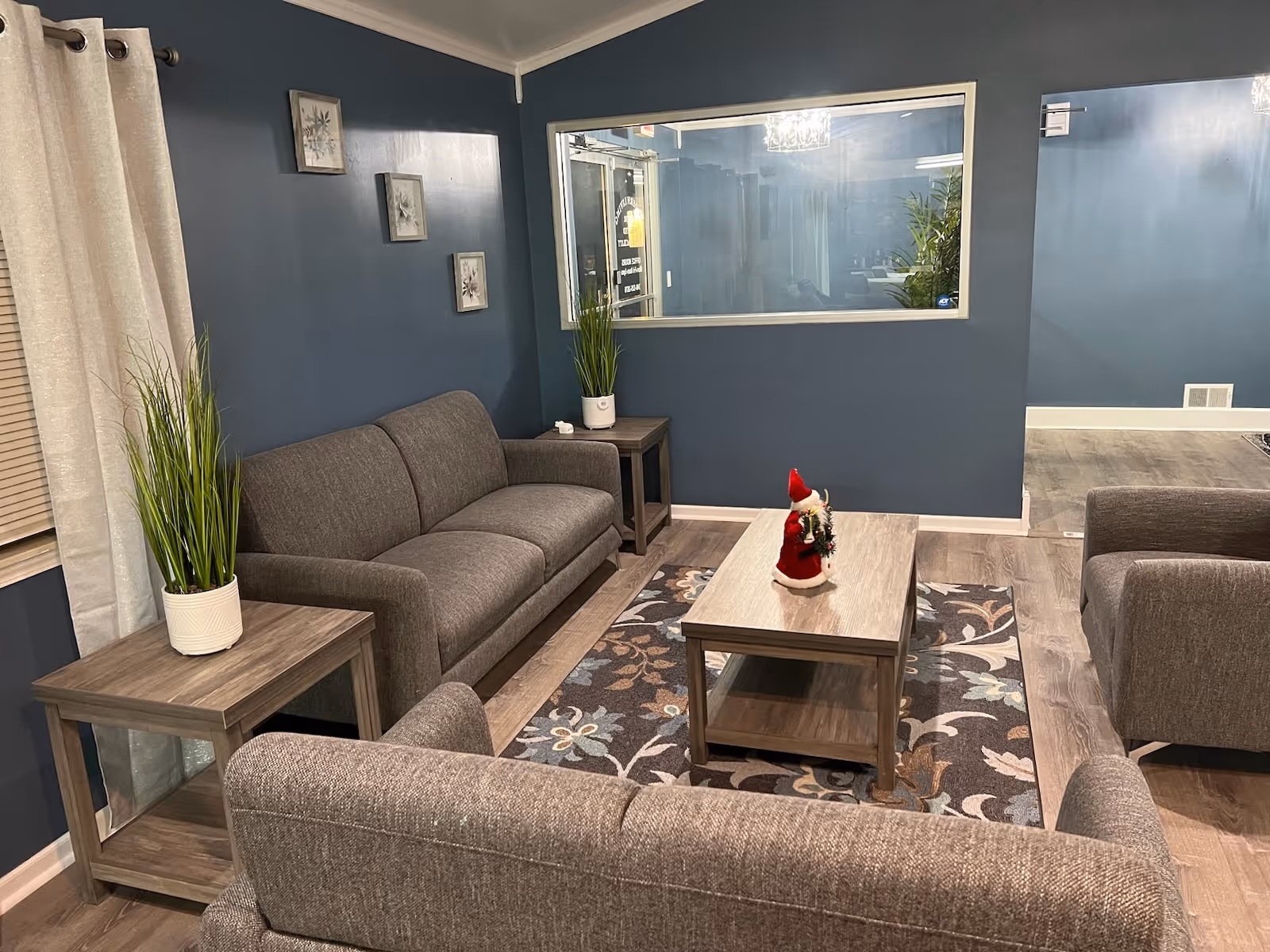 Cozy living room with gray sofas and armchairs around a wooden coffee table on a patterned rug against blue painted walls.