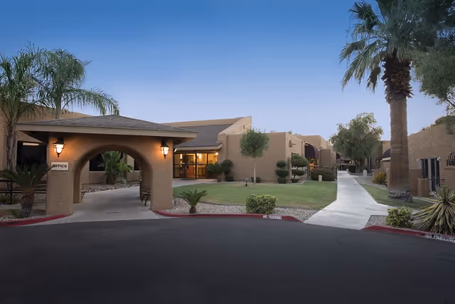 Exterior view of Scottsdale Village Square showing a covered entrance archway, lawn and palm trees with walkways leading to the building.
