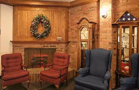 Cozy living room with brick fireplace, wreath, armchairs, and a tall display cabinet.