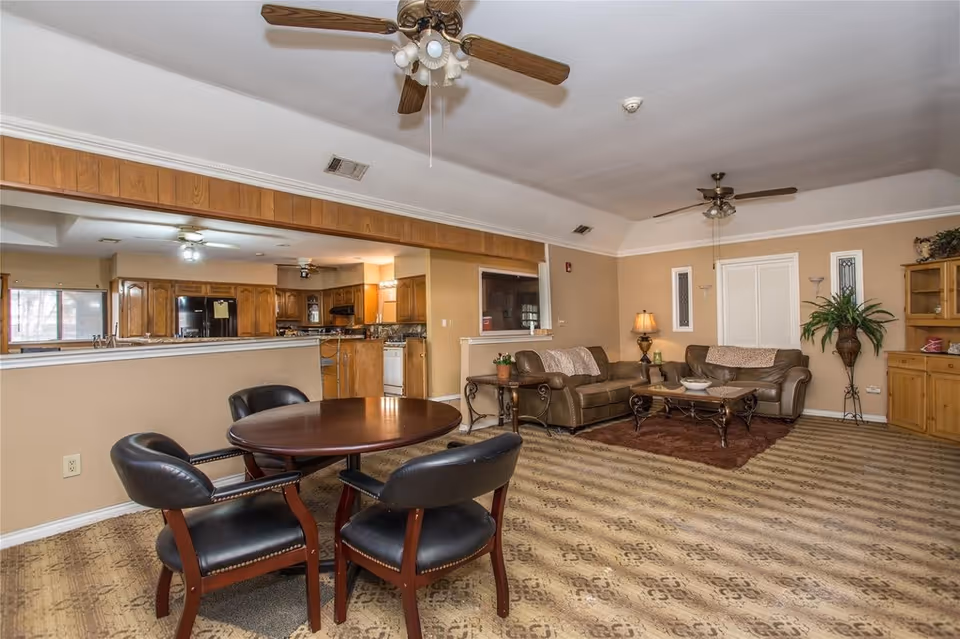 Spacious common living area with leather sofas, a coffee table, a round dining table with four chairs, and an open kitchen in the background.
