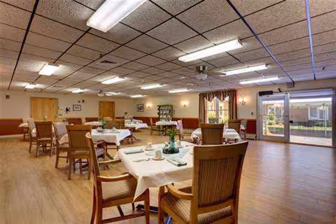 Senior living dining room with multiple tables set for meals and warm lighting