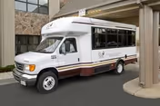 A white and maroon shuttle bus parked under the covered entrance of a senior living facility.