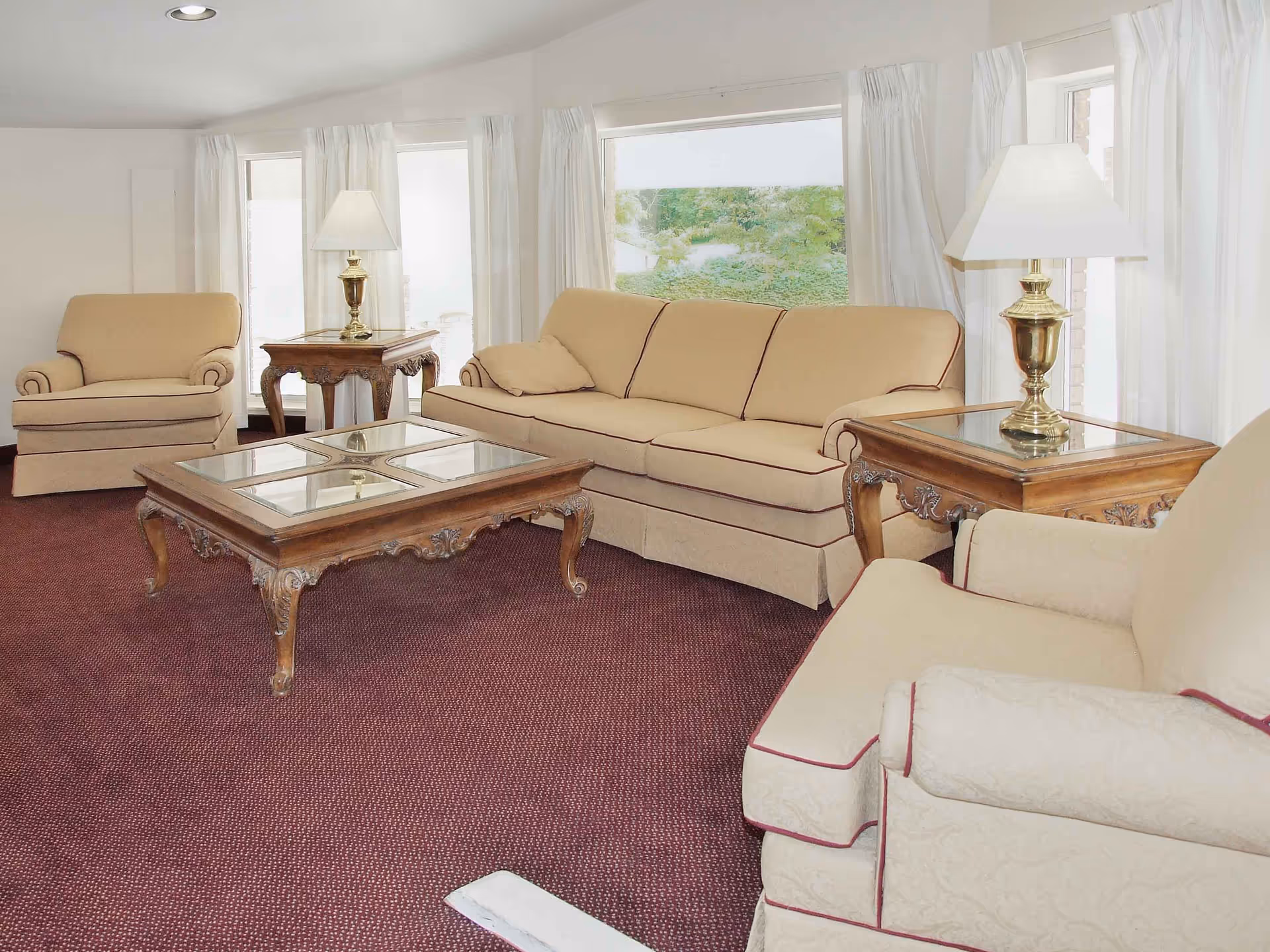 Living room with beige sofa and armchairs, wooden coffee and side tables, lamps, and large windows.