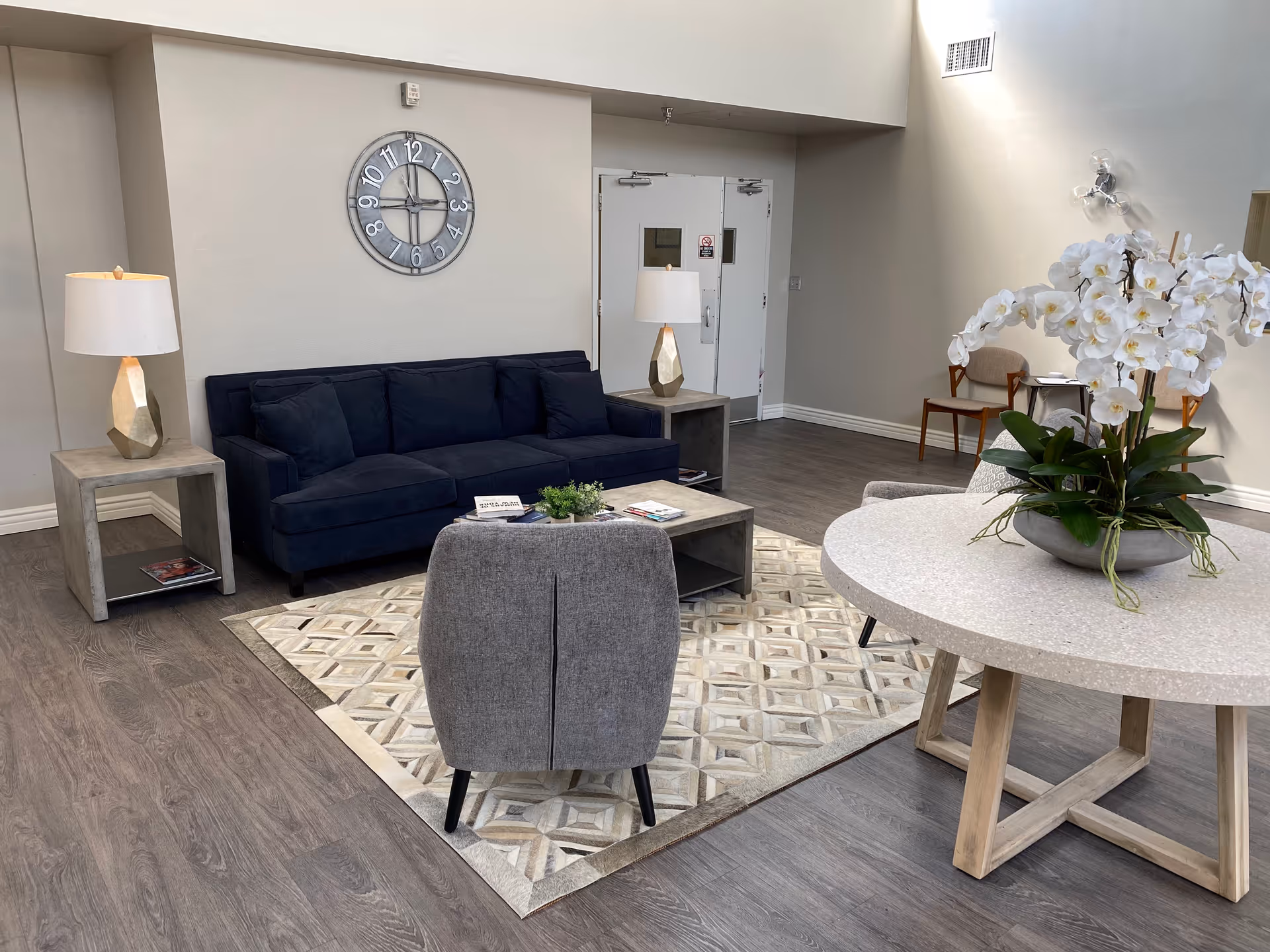 A modern lounge area with a navy sofa, gray armchairs, a coffee table, and a round table topped with white orchids.