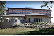 Exterior front view of a multi-story senior living building with a stone terraced lawn, patio umbrellas, and surrounding trees.