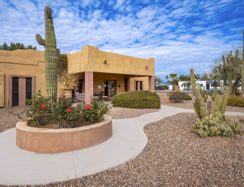 Desert landscaping with cacti surrounds a tan adobe-style building and curved walkway.