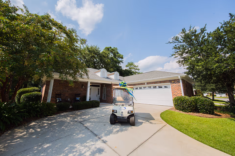 Front exterior of a single-story brick building with a garage, driveway, landscaped lawn and a decorated golf cart parked in front.