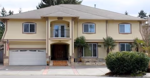 Two-story tan senior care facility exterior with central entry, balcony, and attached garage.