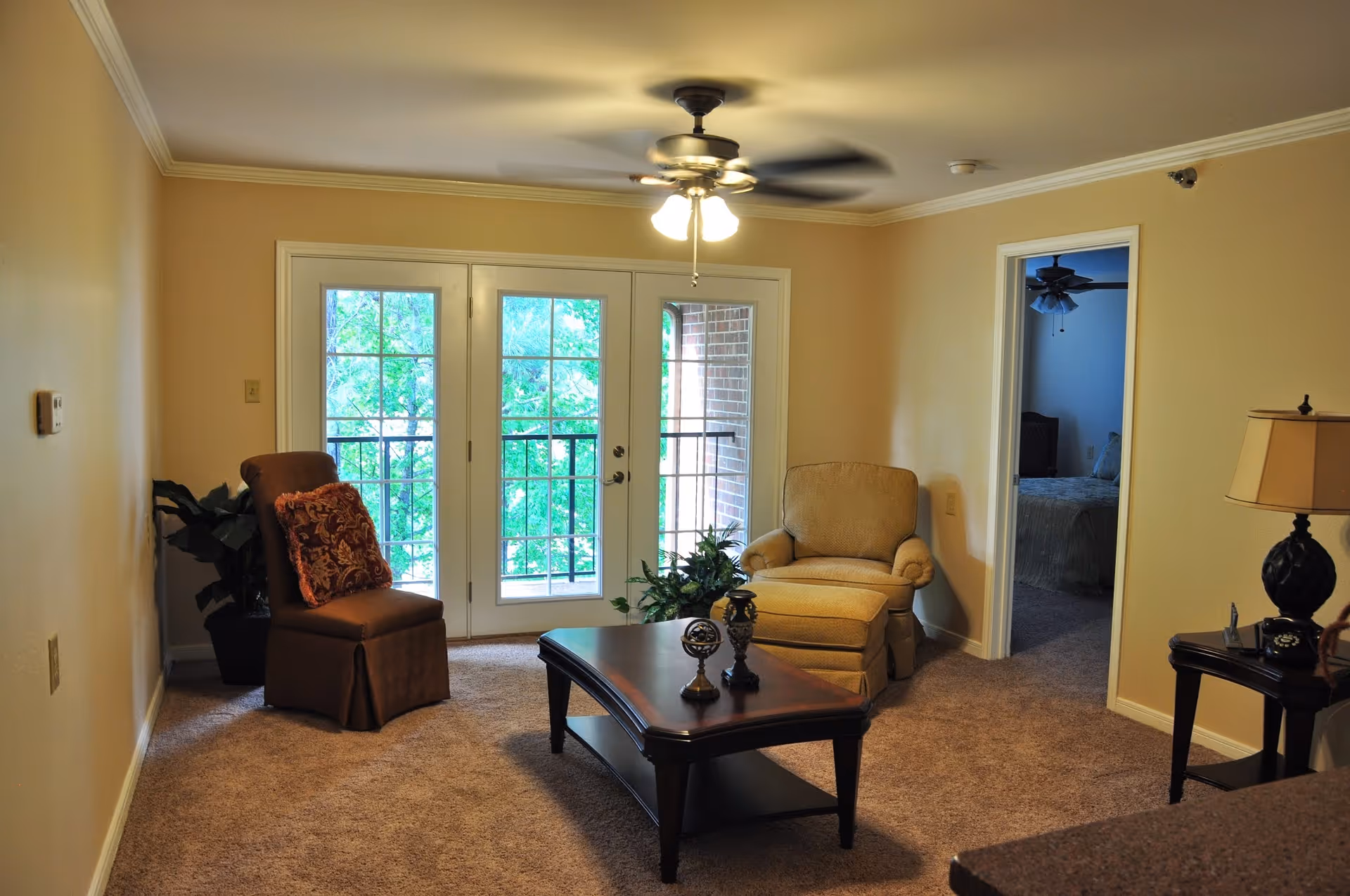 Cozy living room with two armchairs, a coffee table, ceiling fan, and French doors leading to a balcony.