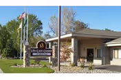 Exterior view of Life Care Center of Richland building with a sign in front displaying the facility name. The building is single-story with a covered entrance, surrounded by trees and a clear blue sky.