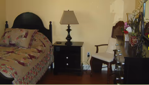 A cozy bedroom in a senior living facility with bed, nightstand, and chair.