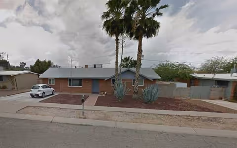Exterior view of a single-story brick building with palm trees and a parked white car.