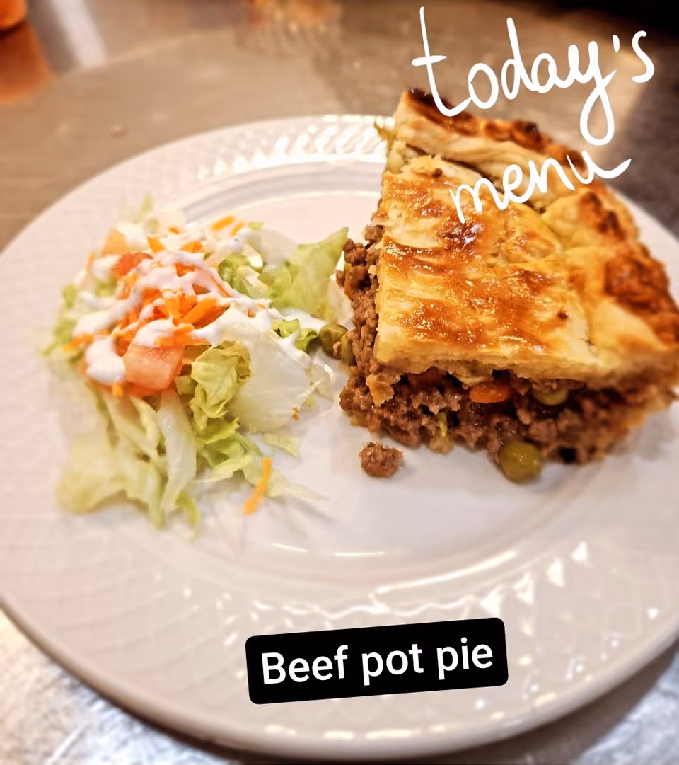 A white plate with a serving of beef pot pie and a side salad consisting of lettuce, shredded carrots, and diced tomatoes topped with a creamy dressing. The image has text overlay that reads 'today's menu' and 'Beef pot pie'.