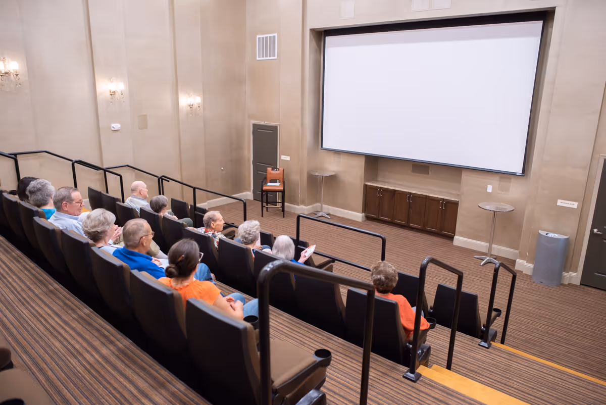 A small auditorium with tiered seating where seniors sit facing a large blank projection screen.