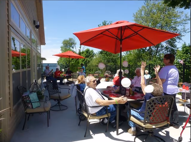 Outdoor patio at Willowick Moments Clinton with elderly residents seated around tables under red umbrellas.