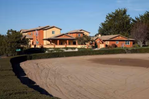 Exterior view of Casa Rosa Elder Care with orange-tan buildings and a curved sandy driveway.