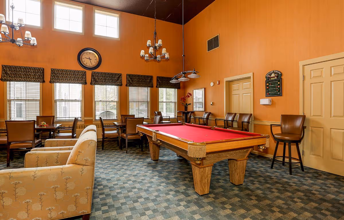 Bright communal lounge with a red-felt pool table, seating and dining tables, and tall windows.