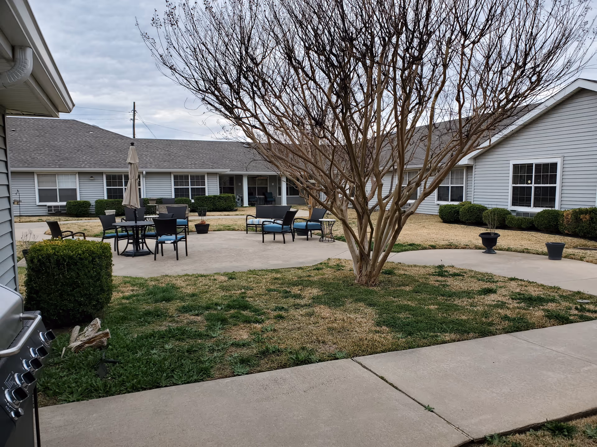 Courtyard at Wildflower Place with patio tables and chairs, a central leafless tree, and surrounding single-story buildings.