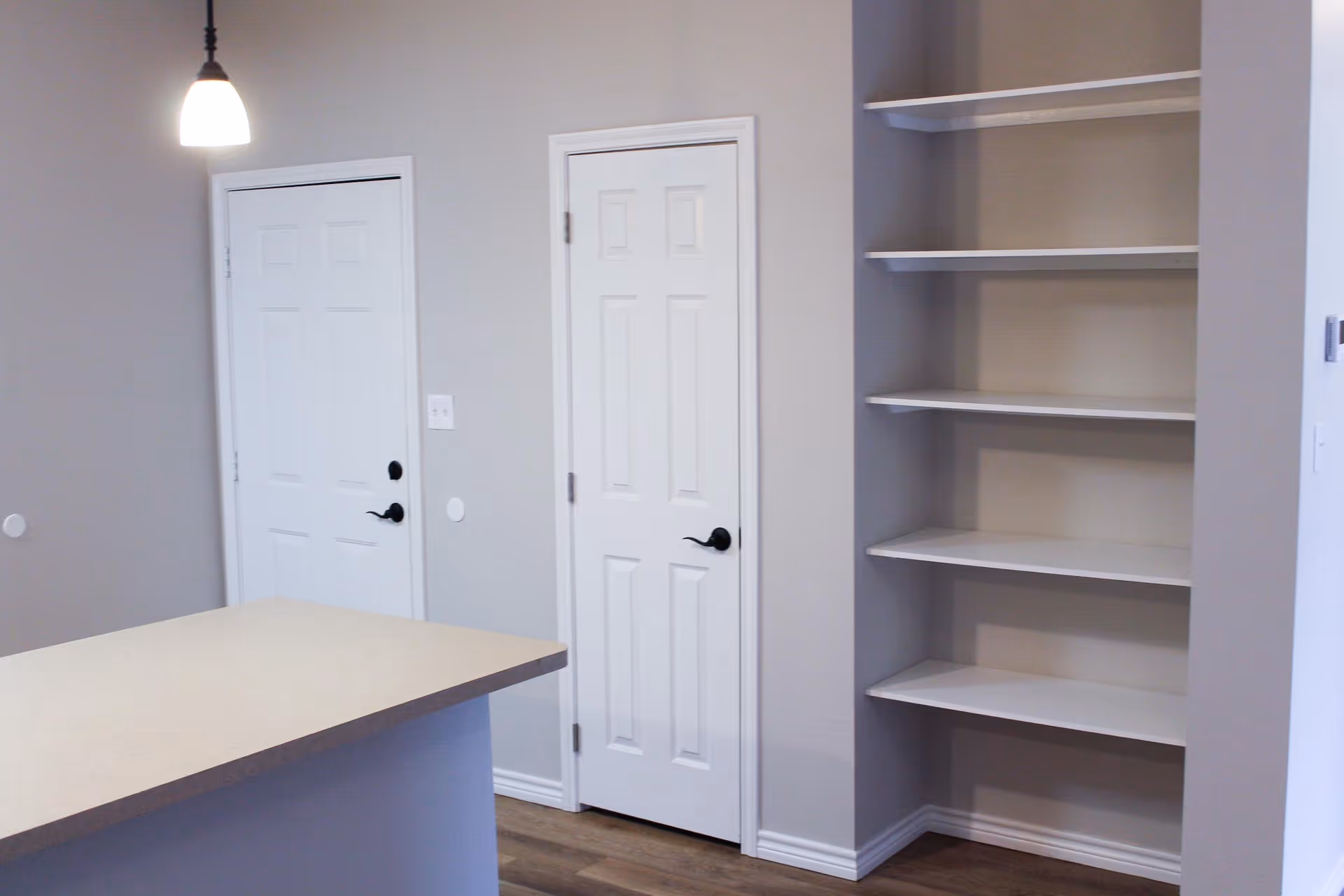 Interior view of a kitchen area with a countertop island, two white doors, and built-in wall shelves.