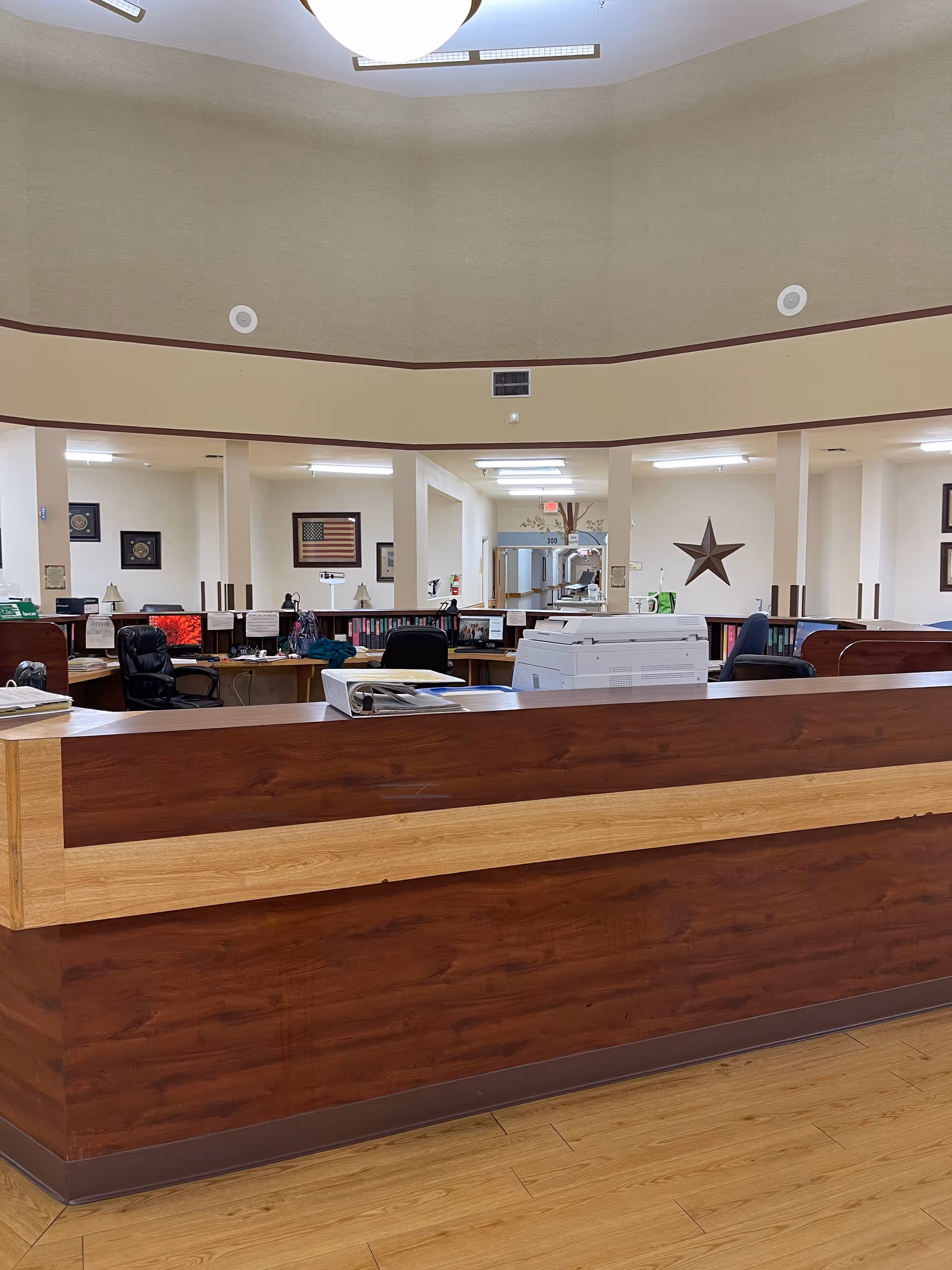 Interior view of a nursing home lobby with a large wooden reception desk and office area in the background.