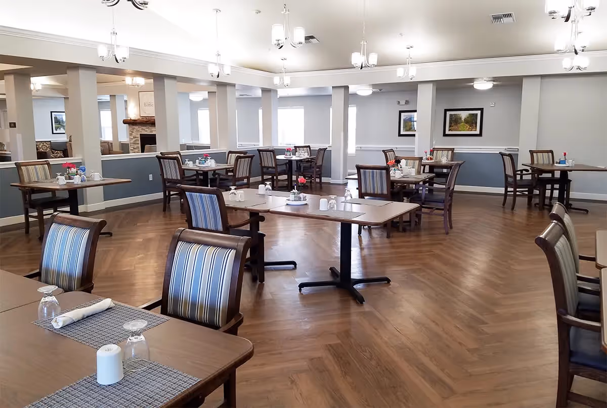 Bright, spacious dining room with several set tables and striped upholstered chairs on wood-patterned flooring.