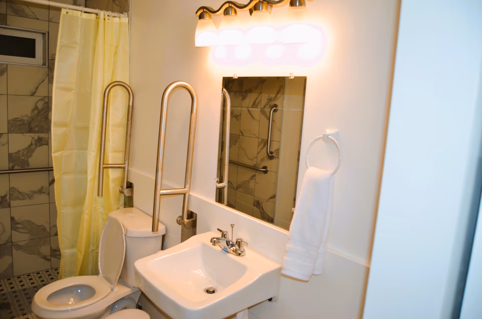 Accessible bathroom with a toilet, sink, mirror, grab bars, and a yellow shower curtain.